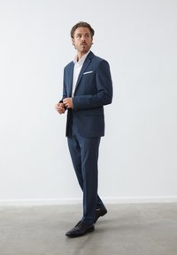 Navyblauw pak met een gestructureerd ontwerp, voorzien van een enkelvoudig pakjasje en slim-fit broek. Witte dressshirt en zwarte schoenen.