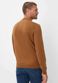 Bruine gebreide trui met lange mouwen en een ronde hals, met ribgebreide mouwen en zoom. De stof heeft een gladde textuur en een aansluitend ontwerp.