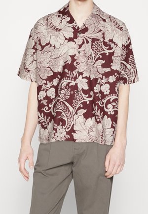 Camicia a maniche corte in bordeaux con motivi floreali e paisley bianchi, dotata di taschino sul petto e chiusura a bottoni. Tessuto morbido.