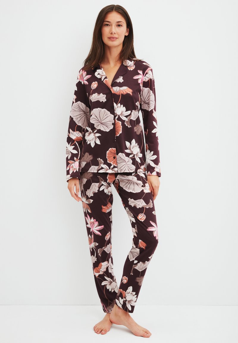 Pyjama set met bloemenprint in donkerpaars, bestaande uit een lange mouwen knoopblouse en bijpassende broek. Zacht materiaal, met grote roze en witte bloemenpatronen.
