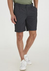 Pantalones cortos gris oscuro de una tela texturizada, con cierre de botón, bolsillos laterales y corte recto, combinados con zapatillas blancas.