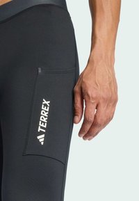 Čierne športové legíny s bočnou vreckom a bielym logom značky "TERREX". Hladká textura, priliehavý strih, viditeľné detaily švov.