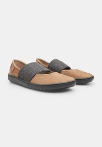 Zapatos marrones de cuero tipo mocasín con una correa de tela gris en el empeine y una suela de goma negra; textura suave con diseño de punta redondeada.