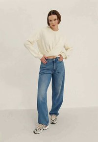 Witte cropped sweatshirt, lichtblauwe losse jeans en meerkleurige sneakers. Soepele stof, relaxte pasvorm, vlakke naden en minimalistisch ontwerp.