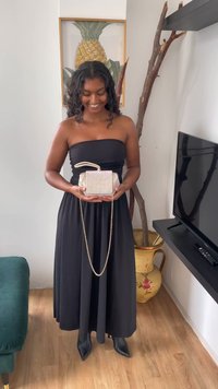 Bolso holográfico de forma rectangular, con detalles metálicos y una correa de cadena, sostenido por una persona que lleva un vestido negro sin tirantes.