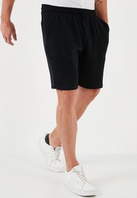 Zwarte, gestructureerde shorts met een relaxte pasvorm, voorzien van een elastische tailleband en zijzakken, gecombineerd met witte sneakers.