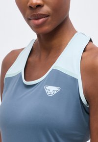 Gros plan d'une personne portant un haut de sport bleu sans manches avec une bordure blanche et bleu clair et un logo de panthère blanche sur la poitrine.