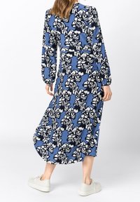 Dlouhé modré šaty s bílým a černým květinovým potiskem, s dlouhými nabíranými rukávy a volným střihem. Kombinované s bílými teniskami pro ležérní vzhled.