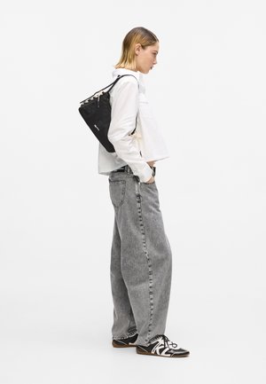 Person wearing white shirt and gray wide-leg jeans with black shoulder bag and black-and-white lace-up shoes, standing sideways.