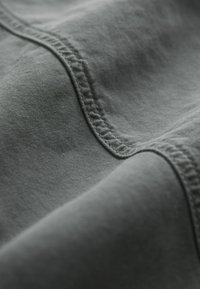 Tissu gris foncé à texture lisse, présentant des coutures plates et des lignes courbes. La surface montre de légères variations et un éclat subtil.