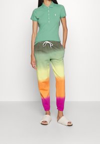 Grön polo skjorta med knappar, kombinerad med gradiente träningsbyxor i grönt, gult, orange och rosa. Vita slip-on skor.