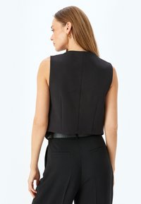 Top noir sans manches au design structuré, doté d'une longueur courte, d'une texture lisse et de plis subtils à l'arrière.