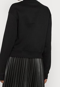 Černá mikina s cropped střihem, žebrovanými manžetami a měkkou texturou, zkombinovaná s černou plisovanou sukní.