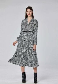 Robe en imprimé zèbre noir et blanc avec des manches longues, un décolleté en V, une taille cintrée et une jupe à volants fluide. Portée avec des bottines noires.