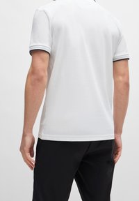 Polo shirt blanc en tissu texturé, avec des manches courtes et des accents bleu marine foncé sur le col et les ourlets des manches.