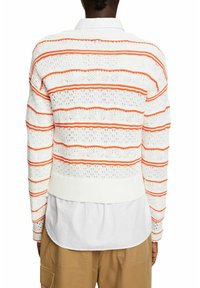 Pull blanc tricoté avec des rayures horizontales orange, présentant un motif texturé et une coupe courte avec un ourlet côtelé. Porté par-dessus une chemise à col.