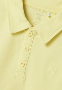Gul polo skjorta med texturerad tyg, två-knapps knäppning och broderad logotyp på bröstet. Har krage och rak nederkant.