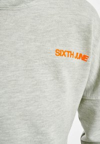 Lys grå hoodie laget av bomull. Har en oransje brodert "SIXTH JUNE"-logo på venstre bryst. Ribbede mansjetter og hals.
