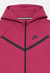 Fukseris fuksijos spalvos su juodais akcentų juostelėmis ir Nike logotipu. Turi gobtuvą ir lygų tekstūrą. Pagrindinė medžiaga pagaminta iš minkštos medžiagos.