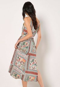 Blumenkleid mit taillierter Taille in Grün, Rot und Weiß; verfügt über dünne Träger und einen mittellangen Rock mit einem seitlichen Schlitz.
