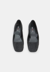 Zapatos planos negros con punta cuadrada, cubiertos de pequeños remaches negros, que cuentan con una amplia banda elástica en la parte superior para un ajuste seguro.