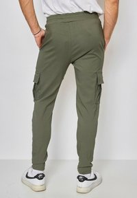 Pantalons cargo vert olive avec taille élastique, poches latérales et coupe fuselée, associés à des baskets blanches avec des accents noirs.