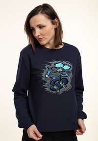 Felpa navy con una grafica di un skateboarder cartoon con un cappellino blu e una tavola da skateboard, che mette in evidenza la texture e la vestibilità rilassata.