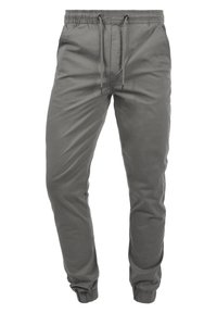Pantalones jogger gris, ajustados en la parte inferior, con cintura elástica, cierre con cordón, bolsillos laterales y puños acanalados. Textura de tela suave y diseño casual.