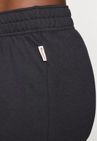 Jogging en coton noir mélangé avec une taille élastique, accompagné d'une petite étiquette beige présentant le logo "Champion" sur le côté.
