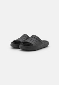 Black slide sandals made of rubber with a textured sole, featuring horizontal ridges and embossed brand logo on the straps.