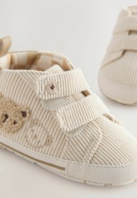 Beez värvi sametist tossud, millel on velcro rihmad, karu brodering ja tekstureeritud pind. Kummist tallad mustriga serva äärde.