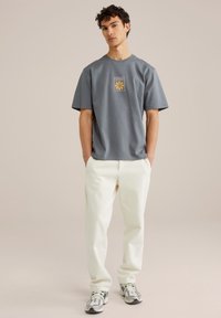Gray short-sleeve t-shirt with a yellow graphic design on the front, paired with white pants and athletic shoes featuring green accents.