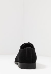 Chaussure habillée en suede noir pour hommes vue de dos sur une surface blanche avec un fond blanc uni.