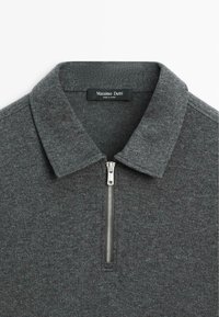 Grauer Pullover mit Reißverschlusskragen, aus strukturiertem Stoff gefertigt. Verfügt über ein kleines Markenetikett im Kragen.
