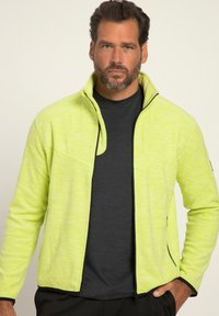 Giacca in pile verde lime con colletto zip, caratterizzata da dettagli neri e una superficie texturizzata, indossata sopra una maglietta grigio scuro.