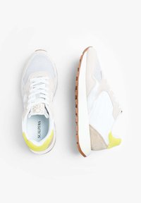 Sneaker con un design in materiali misti bianco, beige e grigio chiaro, con un accento giallo sul tallone e una suola in gomma marrone.