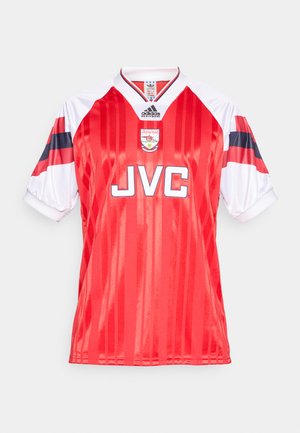 Maglia da calcio rossa con accenti bianchi, strisce verticali e maniche corte. Presenta il logo "JVC" e lo stemma dell'Arsenal sul davanti.