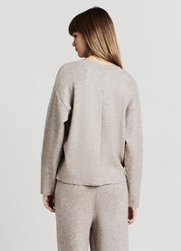 Beiger Damenpullover mit lockerem Schnitt, geripptem Kragen und weichem, strukturiertem Stoff, kombiniert mit passenden Hosen.