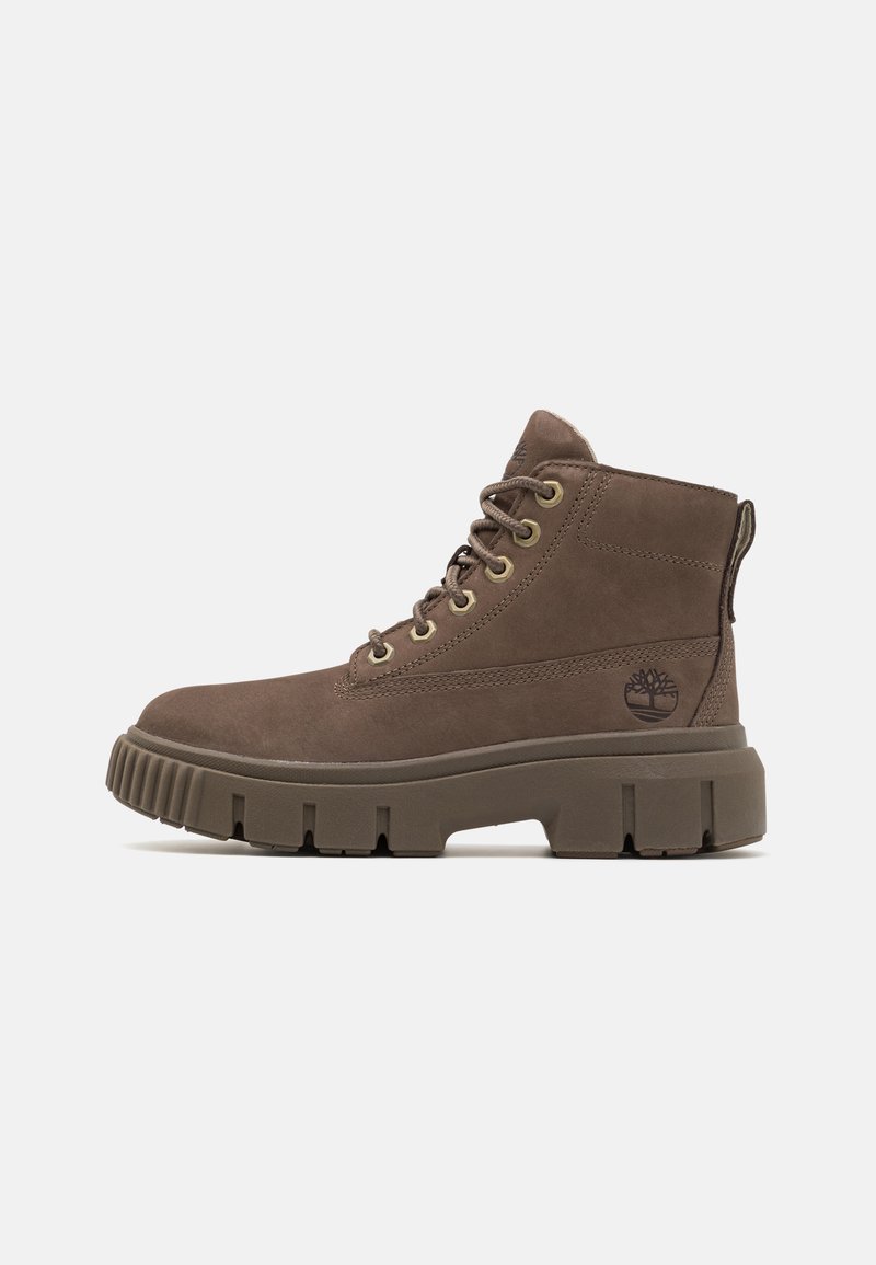 Stivale alla caviglia in suede marrone con punta tonda, sistema di allacciatura, occhielli dorati e suola in gomma spessa. Presenta il logo sul lato e un colletto imbottito.