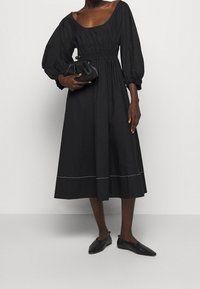 Svart klänning i midilängd med puffärmar, elastisk midja och rundad uringning. Slät tyg med subtila vita sömmar vid fållen.