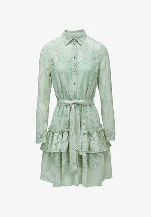 Abito di pizzo verde chiaro con maniche lunghe, davanti con bottoni, cintura annodata in vita e orlo a balze sovrapposte.