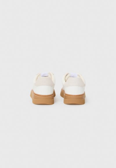 Baskets blanches avec une tige lisse en simili cuir et des accents beiges, dotées d'une semelle en gomme, d'une forme arrondie et d'un col rembourré.