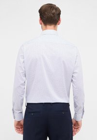 Camicia da uomo a maniche lunghe bianca con motivo a quadri blu; presenta un colletto button-down e polsini a barile; abbinata a pantaloni scuri.