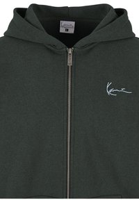 Mørkegrønt zip-up hættetrøje lavet af blødt stof, har en frontlynlås og et broderet logo på venstre bryst. Justerbar snor i hætten.