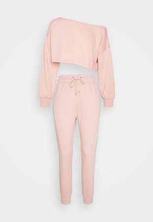 Lichtroze tweedelige outfit met een off-shoulder cropped top met lange mouwen en joggerbroeken met elastische tailleband en trekkoord op een effen achtergrond.
