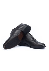 Scarpe in pelle nera con dettagli brogue, design con lacci, punta appuntita e suola in gomma testurizzata. Accenti marroni nel tallone e nella soletta.
