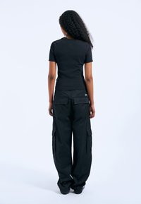 Czarna dopasowana koszulka typu t-shirt w połączeniu z luźnymi czarnymi spodniami cargo z bocznymi kieszeniami i tylną kieszenią naszywaną. Gładka faktura materiału.