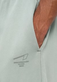 Hellgrüner Sweatshirt mit weicher Textur, ausgestattet mit einer seitlichen Tasche und einem dezenten, geprägten Logo entlang der Naht. Lässiges Design, minimale Akzente.