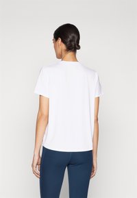 Kortermet, hvit T-skjorte med rett snitt, rund hals og glatt tekstur. Brukt med blå leggings.