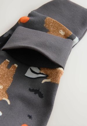 Chaussettes grises avec des motifs d'animaux amusants, présentant des ours bruns, des chauves-souris noires et des pois oranges, retroussées au niveau du poignet.